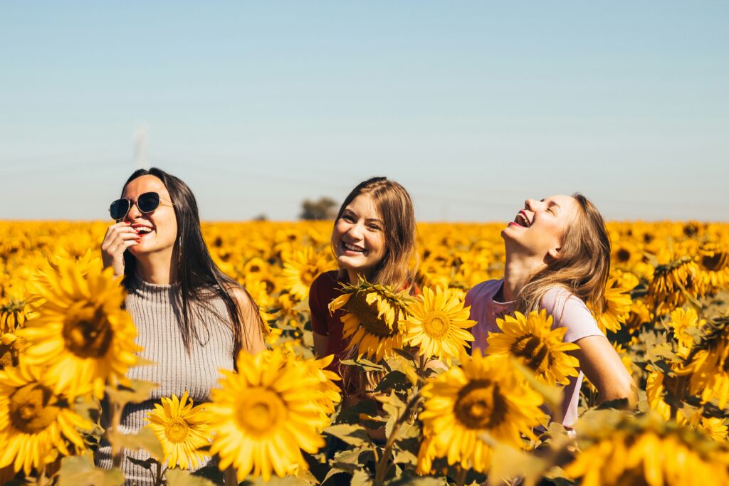 Drei Frauen stehen in einem Sonnenblumenfeld und haben Spaß. Bild zum Blog: The beauty of a woman.