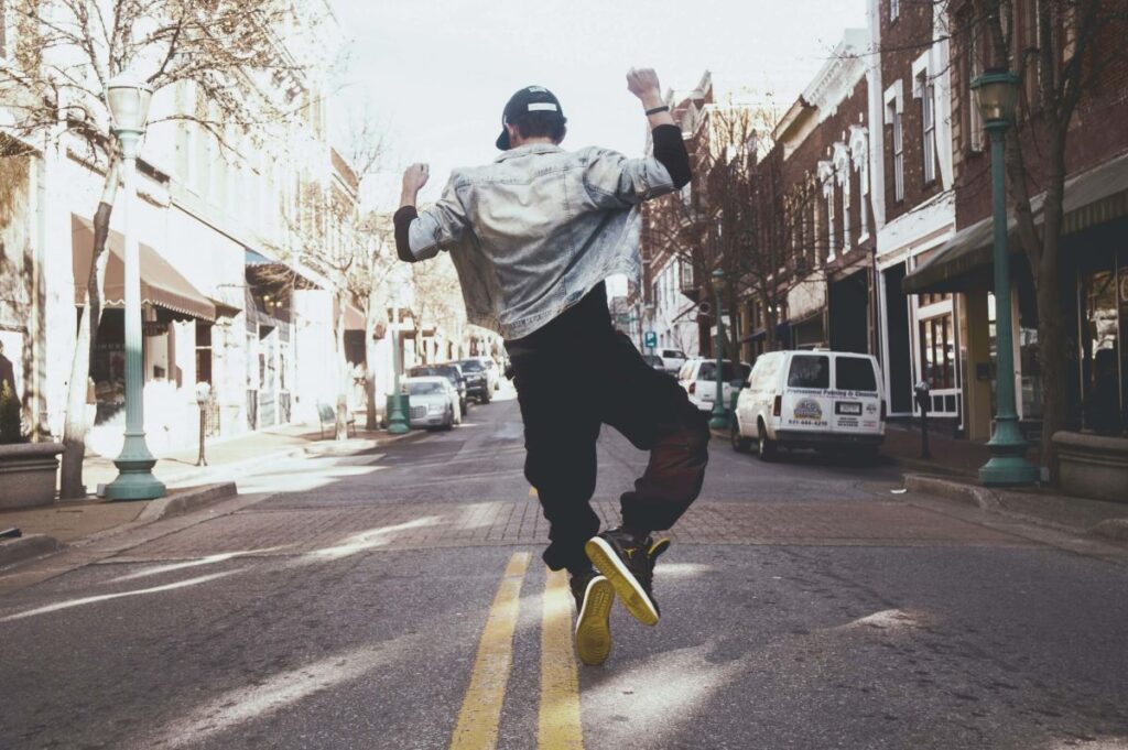 Ein Mann hüpft vor Freude. Er steht auf einer Straße. Bild zum Blogartikel: Versuch's doch mal mit Gelassenheit