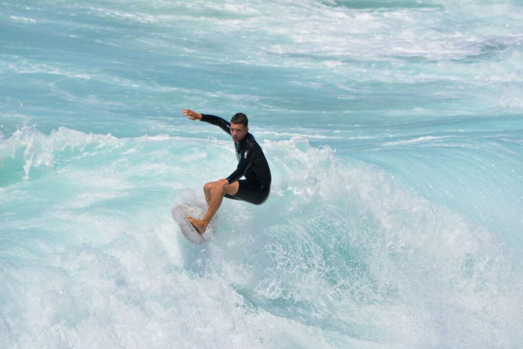 Ein Surfer reitet eine hohe Welle. Das Meer ist klar und türkisblau.