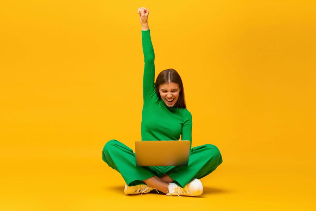 Der Hintergrund ist orange-gelb. In der Mitte sitzt eine grün gekleidete Frau in im Schneidersitz. Sie hat ein Notebook bei sich und hält ihren rechten Arm in die Höhe.